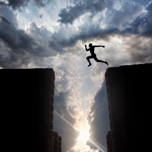 Man Silhouette jumping over the abyss at sunset cloudy sky background